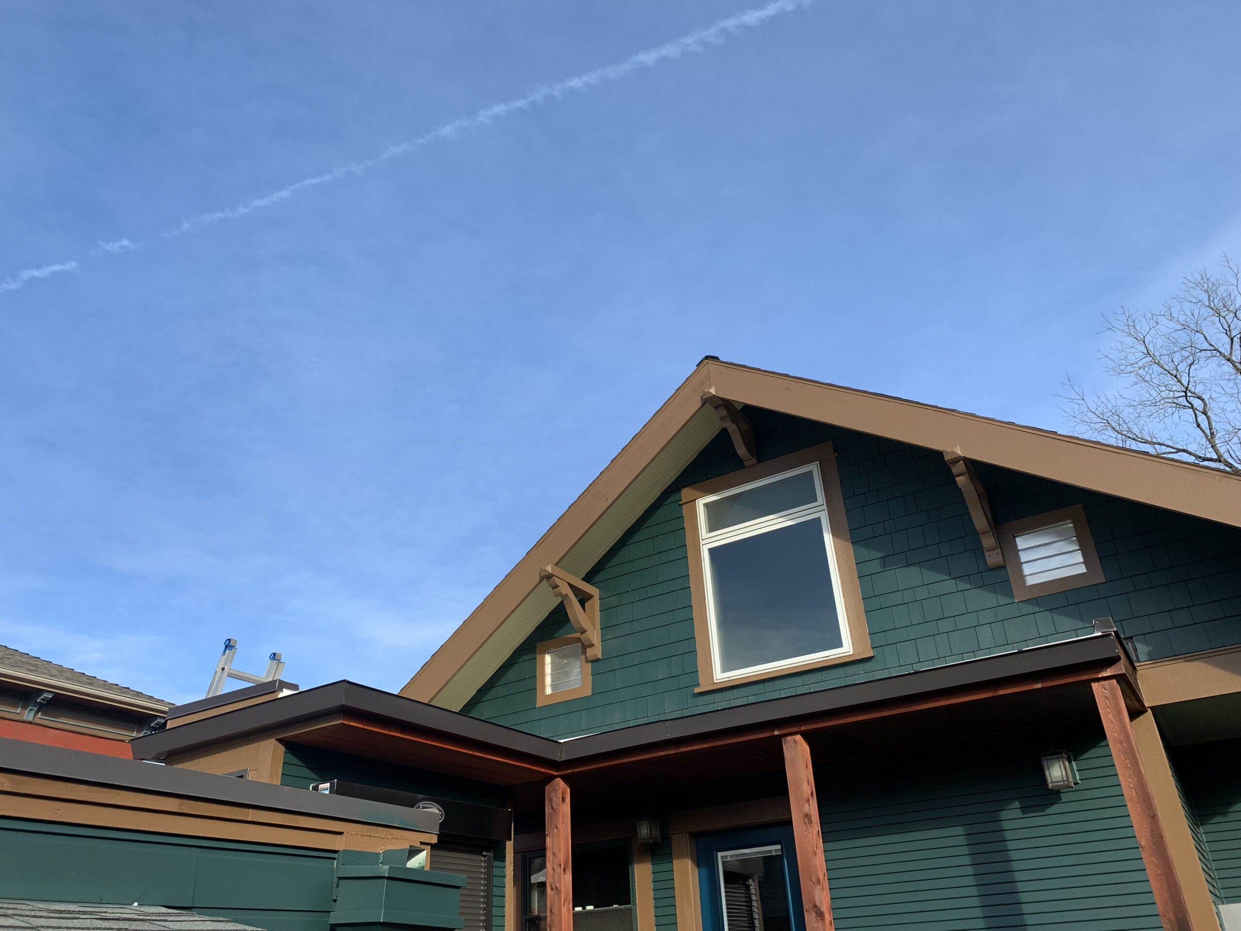 Exterior view of a green and brown house with a triangular roof against a clear blue sky.